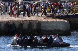 Lampedusa estate 2000. Un gommone carico di immigrati entra in porto sotto gli occhi dei turisti, mentre altri immigrati, arrivati nei giorni precedenti si imbarcano sul traghetto per Porto Empedocle. ©REUTERS/Tony Gentile